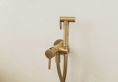 Stylish brass bidet shower on wall, modern bathroom design detail close up.Handle water sprayer, bathroom interior element. Hygiene concept